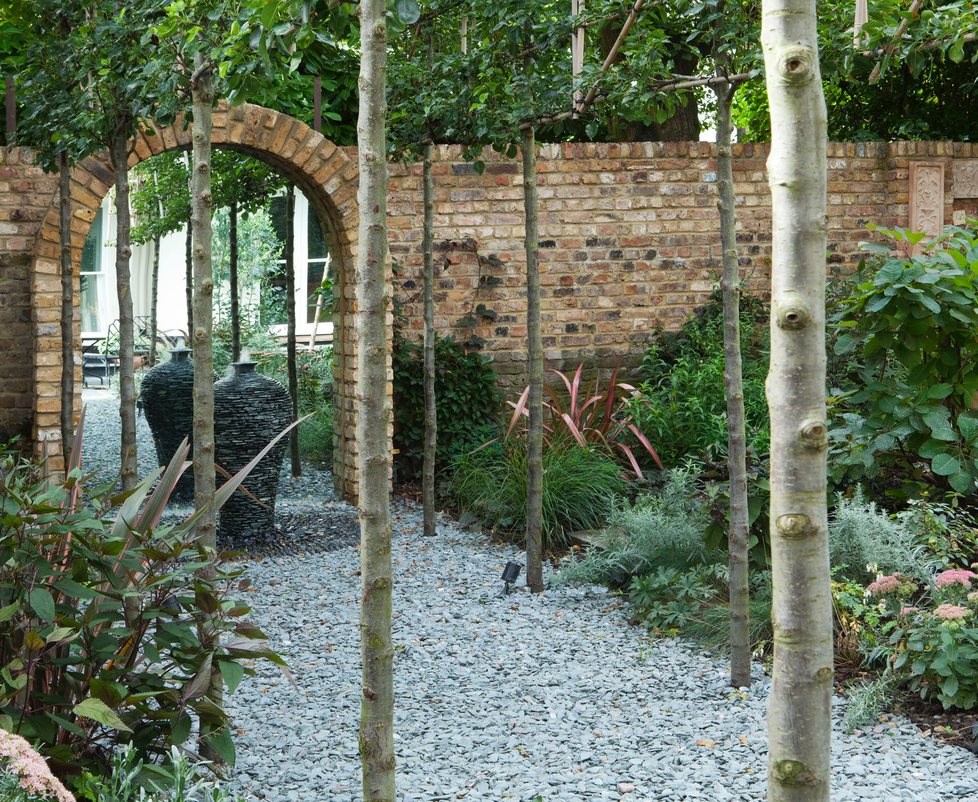 An avenue of pleached Pyrus, leads you to the mirrored arch and water feature.