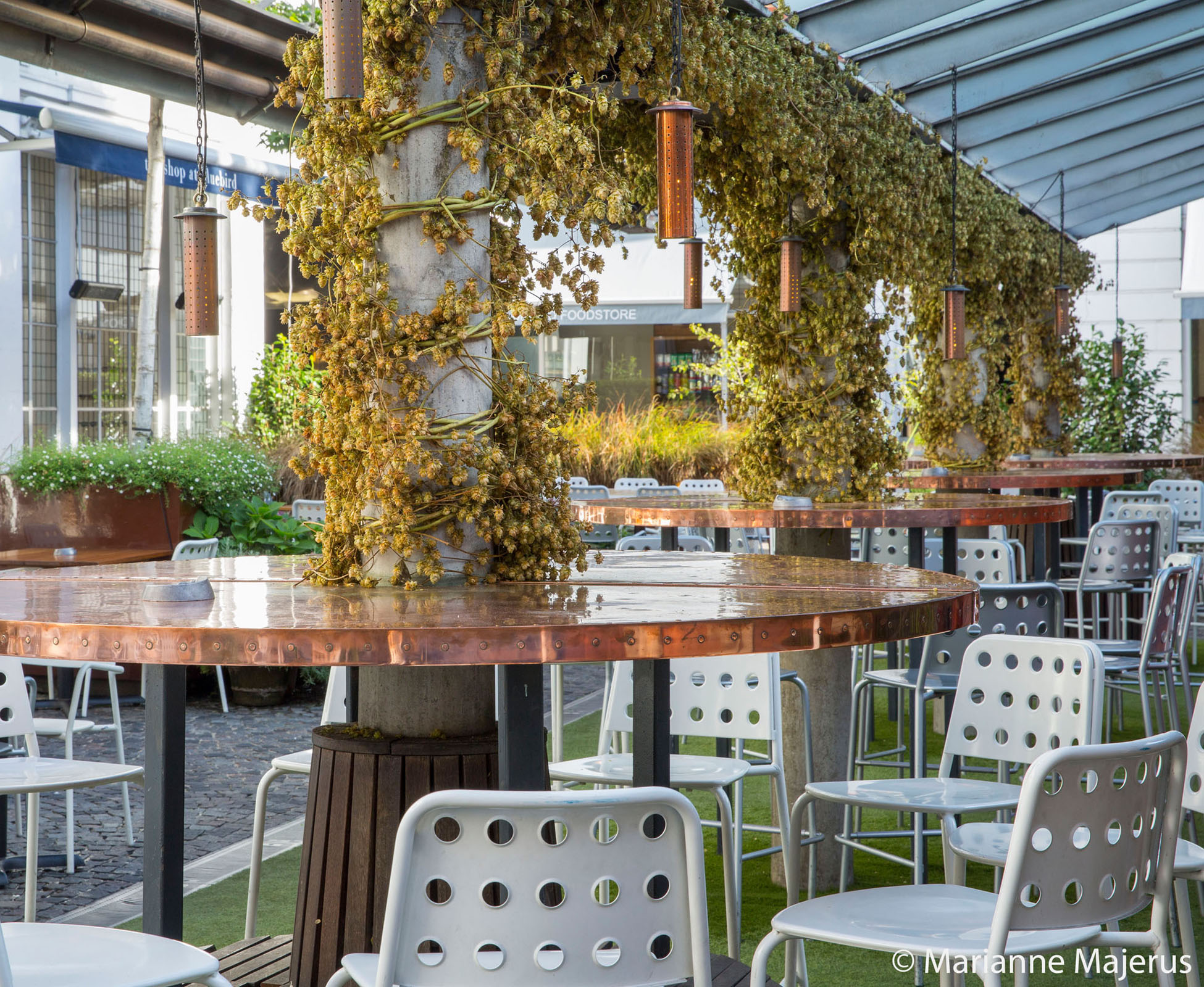 View of the covered pergola in Bluebird’s courtyard with its new copper tables and hanging copper light, for a warm light atmosphere, night and day.