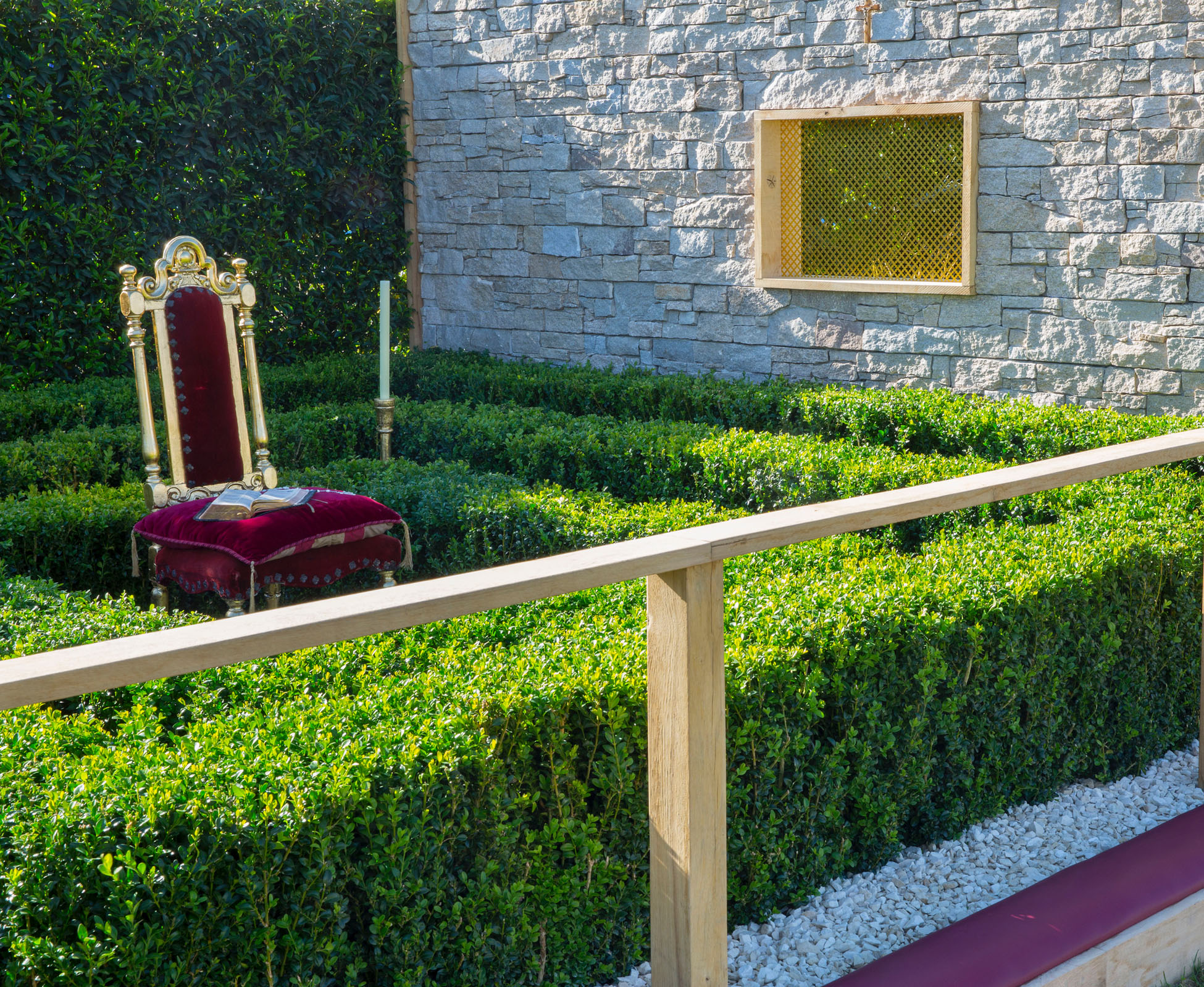 The red velvet chair in the controlled garden is surrounded by clipped evergreen box hedges.