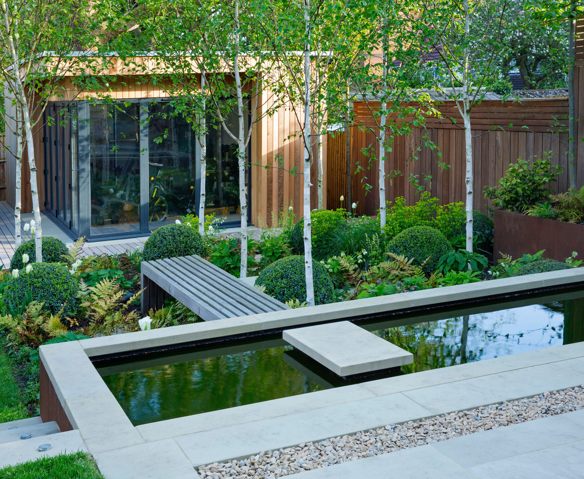 The stepping stone above the water is a great invite to walk through the woodland planting, on the hardwood boardwalk, when going to the outdoor gym in this Highgate garden.