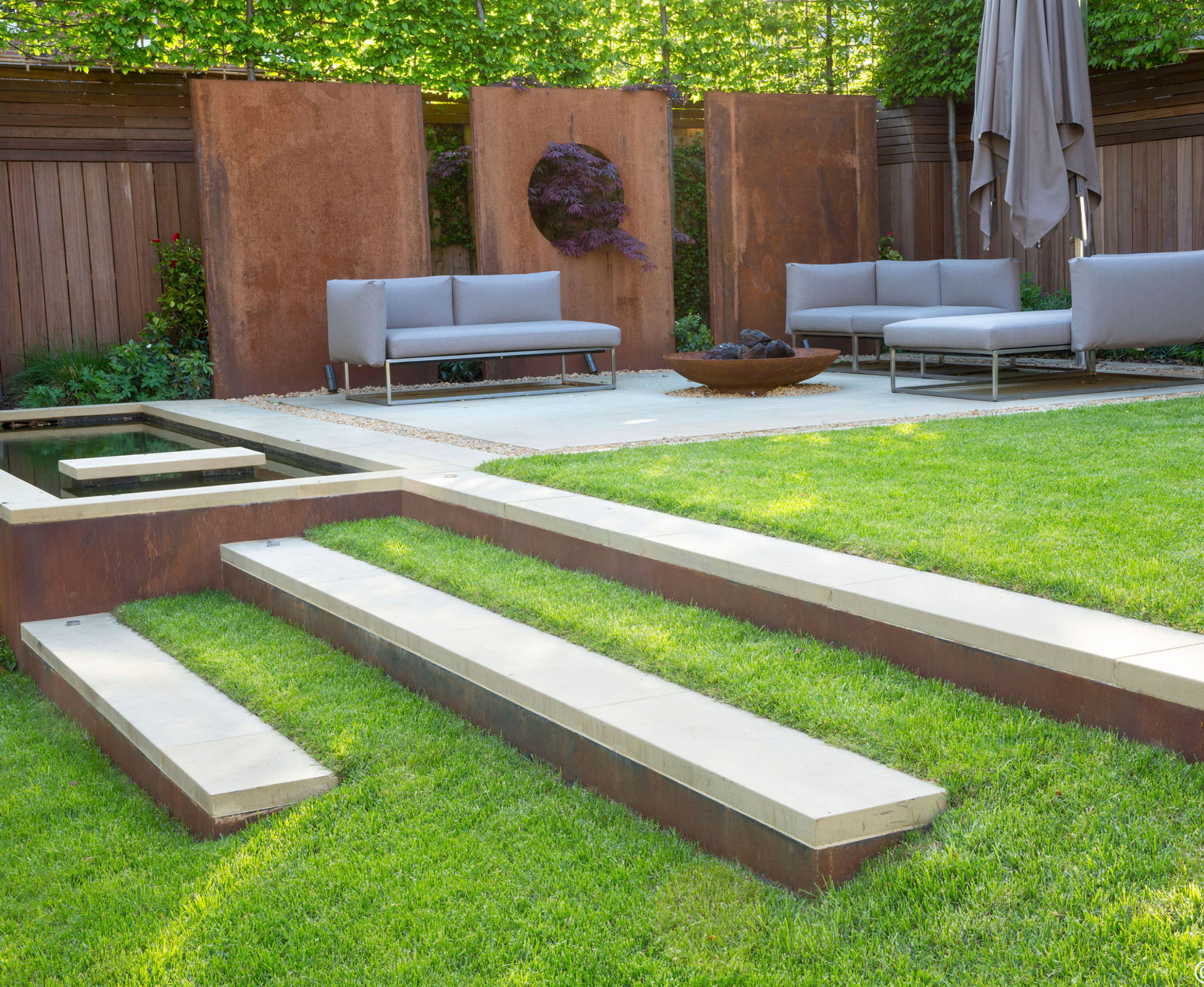 The sandstone and corten steps in the lawn follow the existing slope in this Highgate garden to lead to the cosy outdoor lounge.