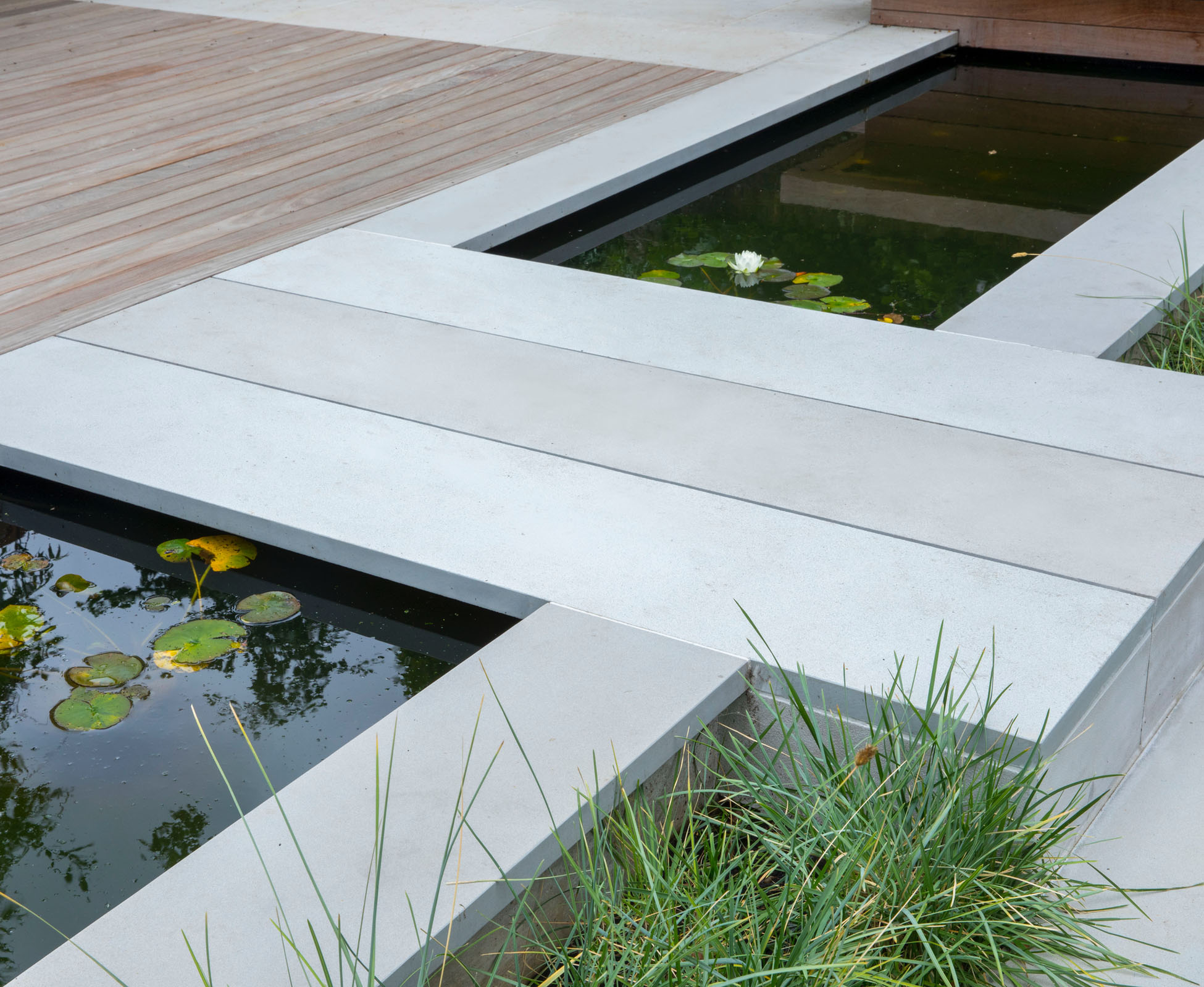 Detail of the sandstone bridge over the black water and waterlilies. The hardwood deck and built in bench contrast nicely with the soft grey of the stone in this Islington garden.